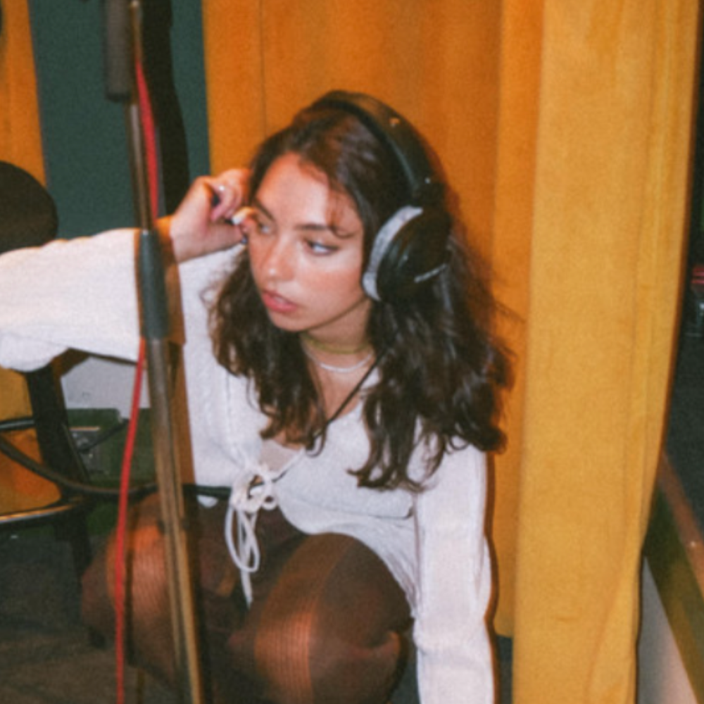 Woman with headphones crouched by a microphone stand in a studio booth