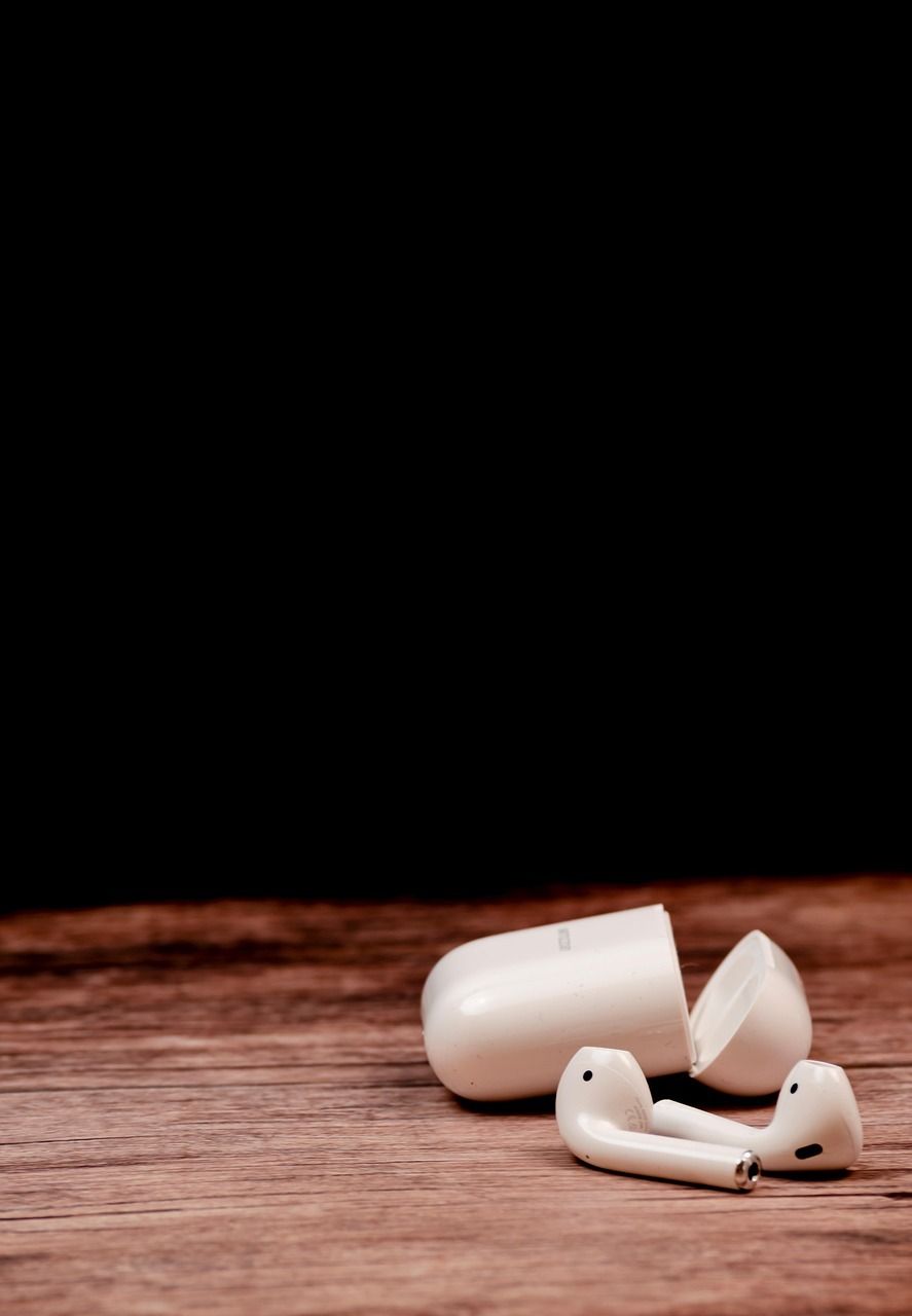 White wireless earbuds and their open case on a wooden table