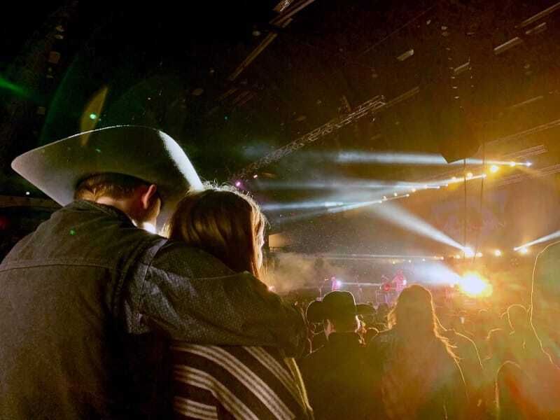 Couple in a cowboy hat watching a stage lit up at a country concert