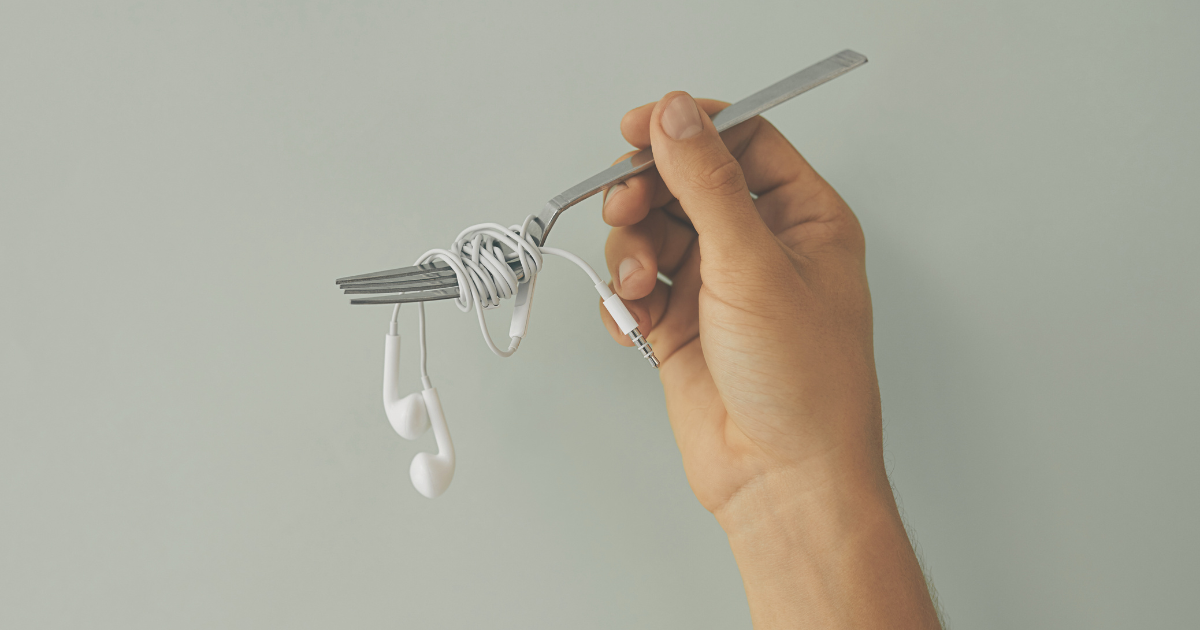 Hand holding a fork with white earphones twirled round it like spaghetti, for 'Your Taste In Music Sucks'