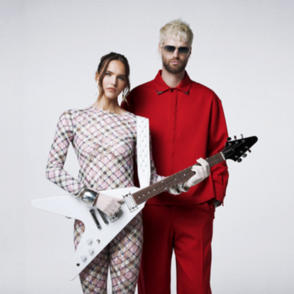 SOFI TUKKER - Sophie in a checked catsuit with a white guitar, Tucker in a red suit and sunglasses