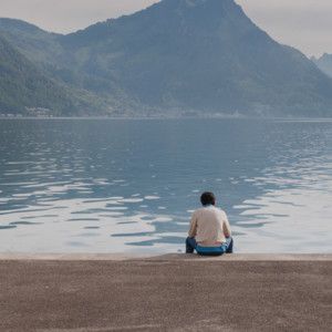 Cover for the Embracing the Loneliness playlist - a person sitting alone at the edge of a mountain lake