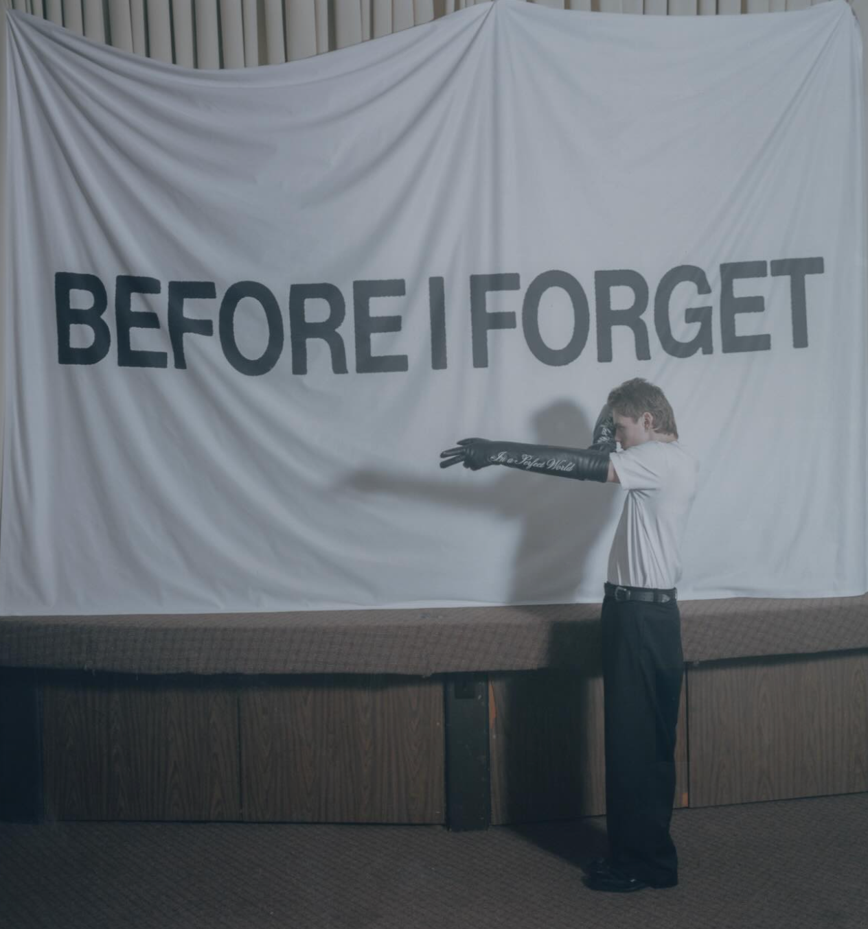 The Kid LAROI pointing at a banner reading BEFORE I FORGET in an empty hall