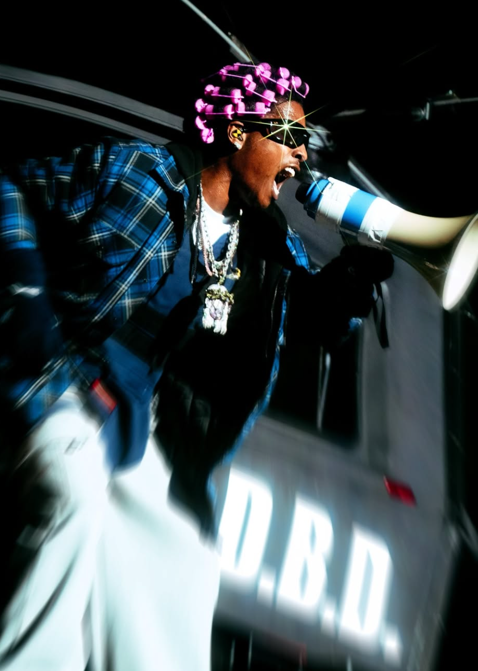 A$AP Rocky shouting into a megaphone on stage, wearing pink hair rollers