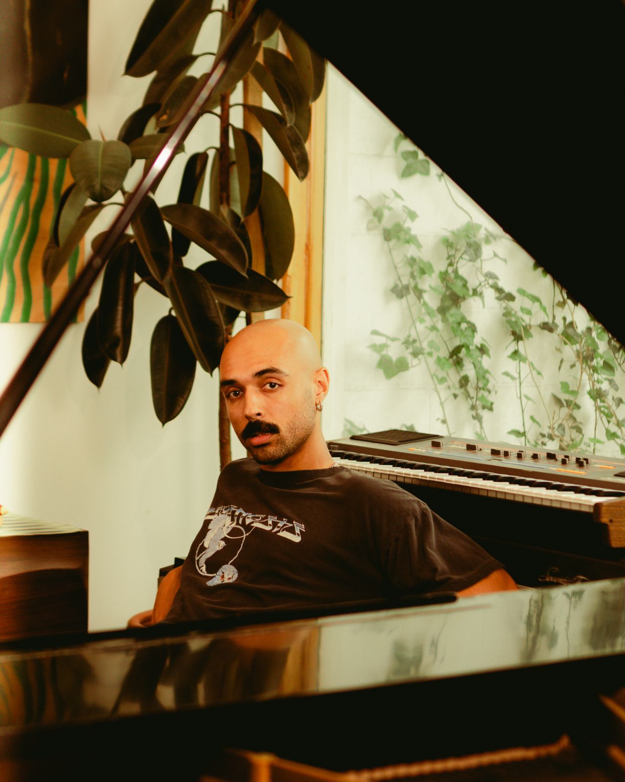 Deion Gill seated at a grand piano among house plants
