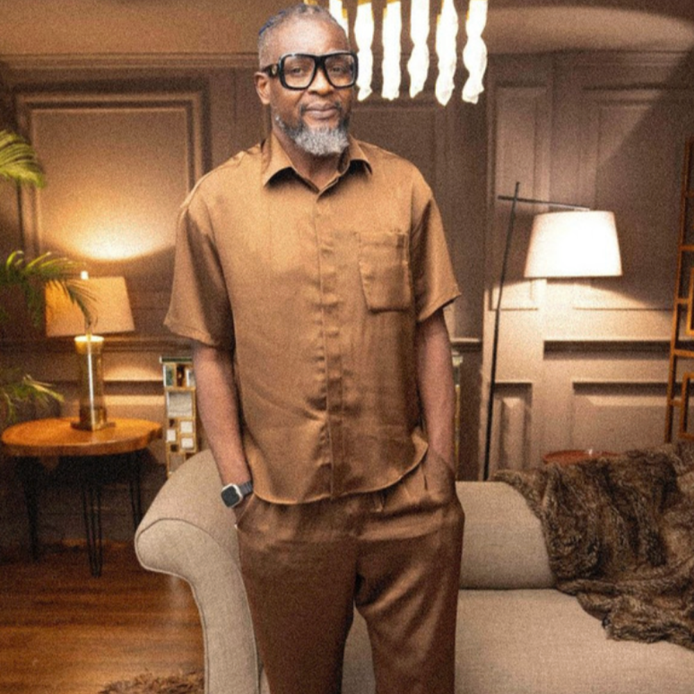 Miki Ikhifa in a tan shirt and trousers in a lamplit living room