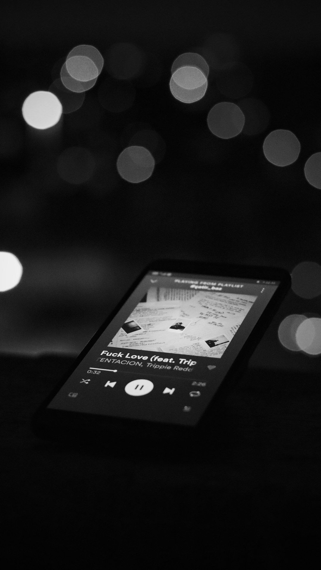 Phone playing a track on a dark table, bokeh lights behind, in black and white