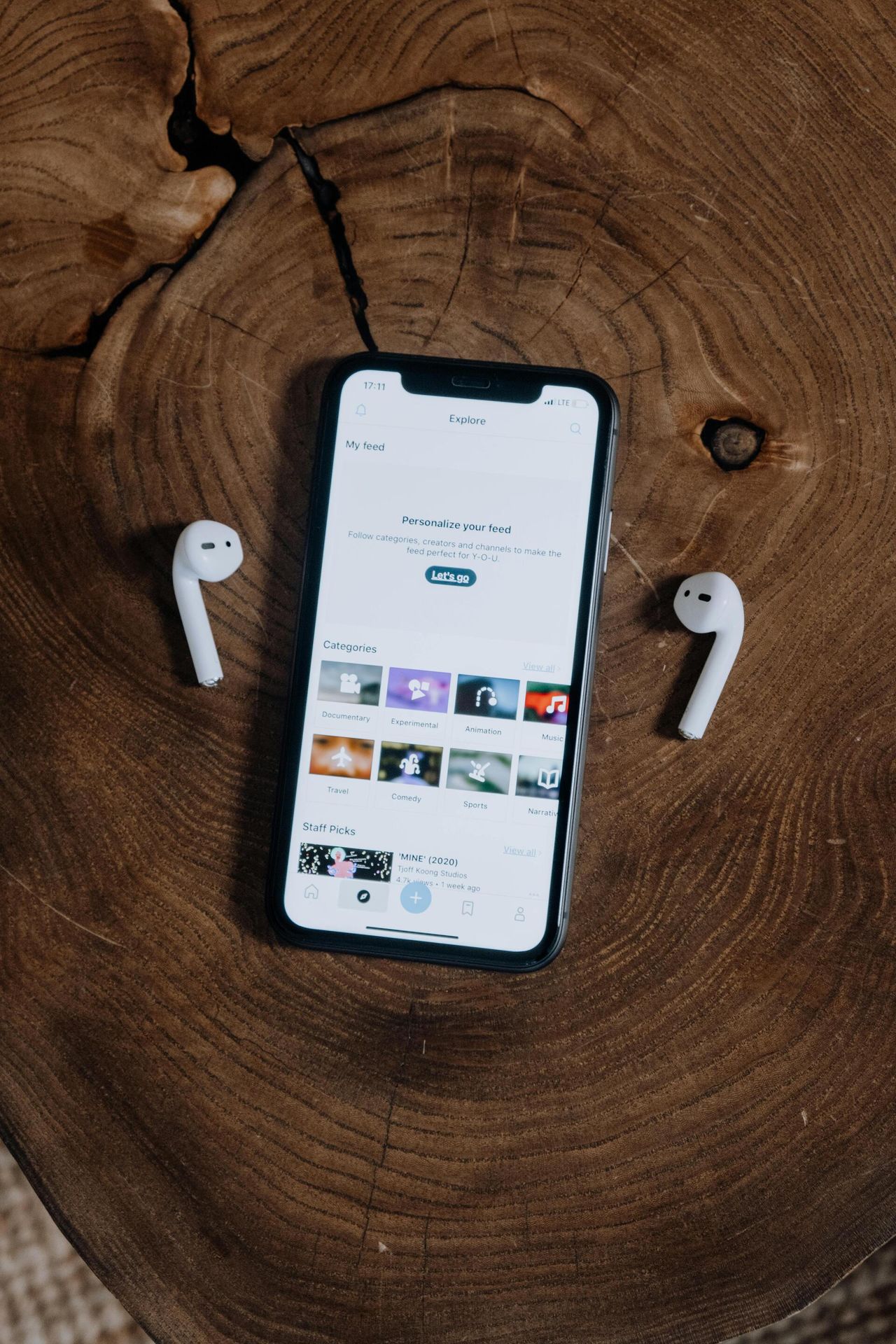 Phone showing a music app on a tree stump, with AirPods either side