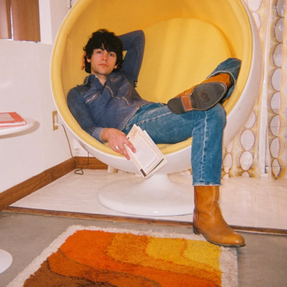 Max reclining in a yellow egg chair with a book