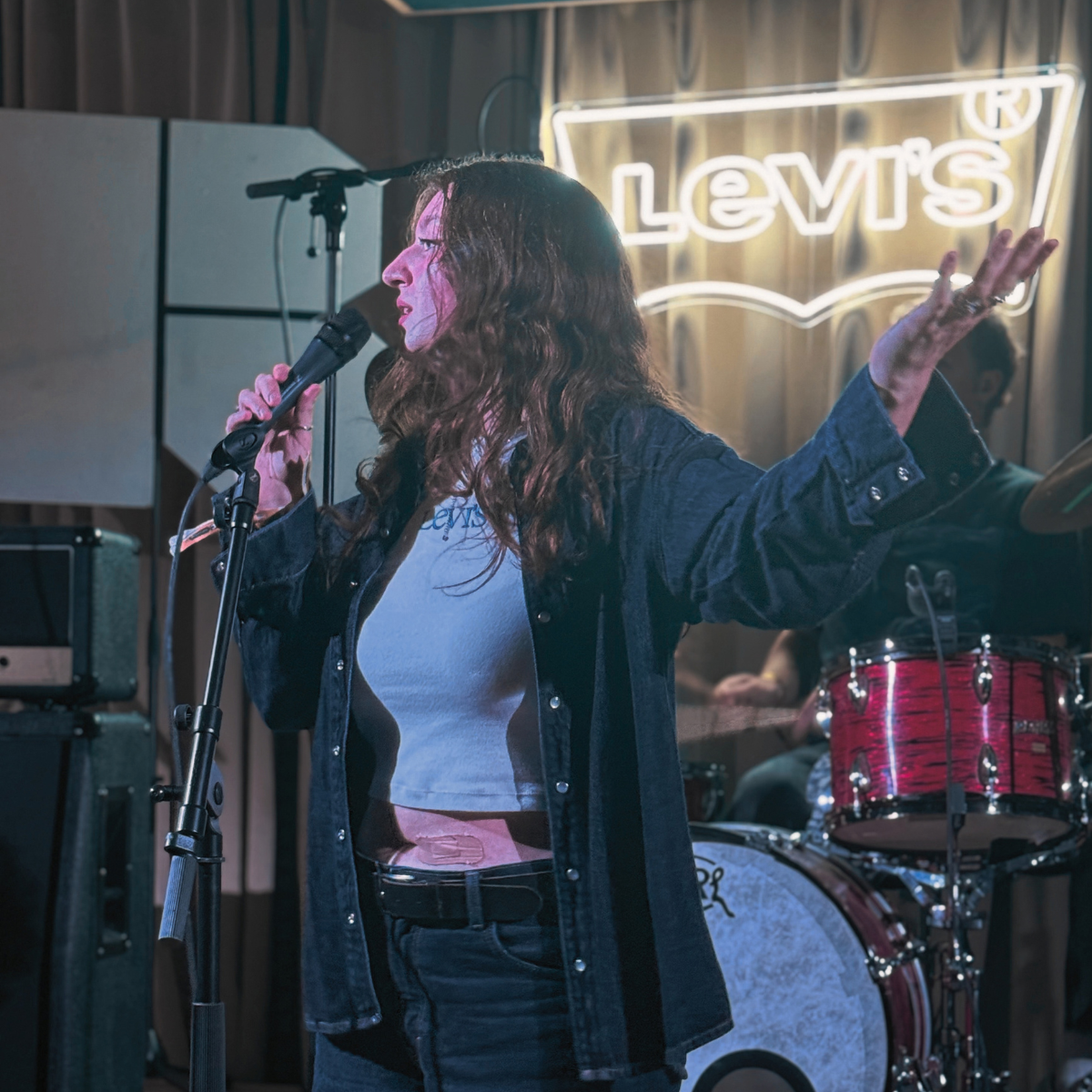 Mia singing with one arm outstretched in front of a neon Levi's sign