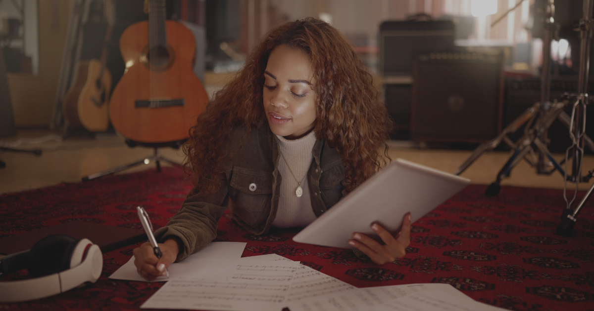 Woman writing lyrics on the floor of a room full of guitars
