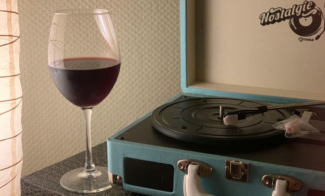 Glass of red wine beside a turquoise suitcase record player