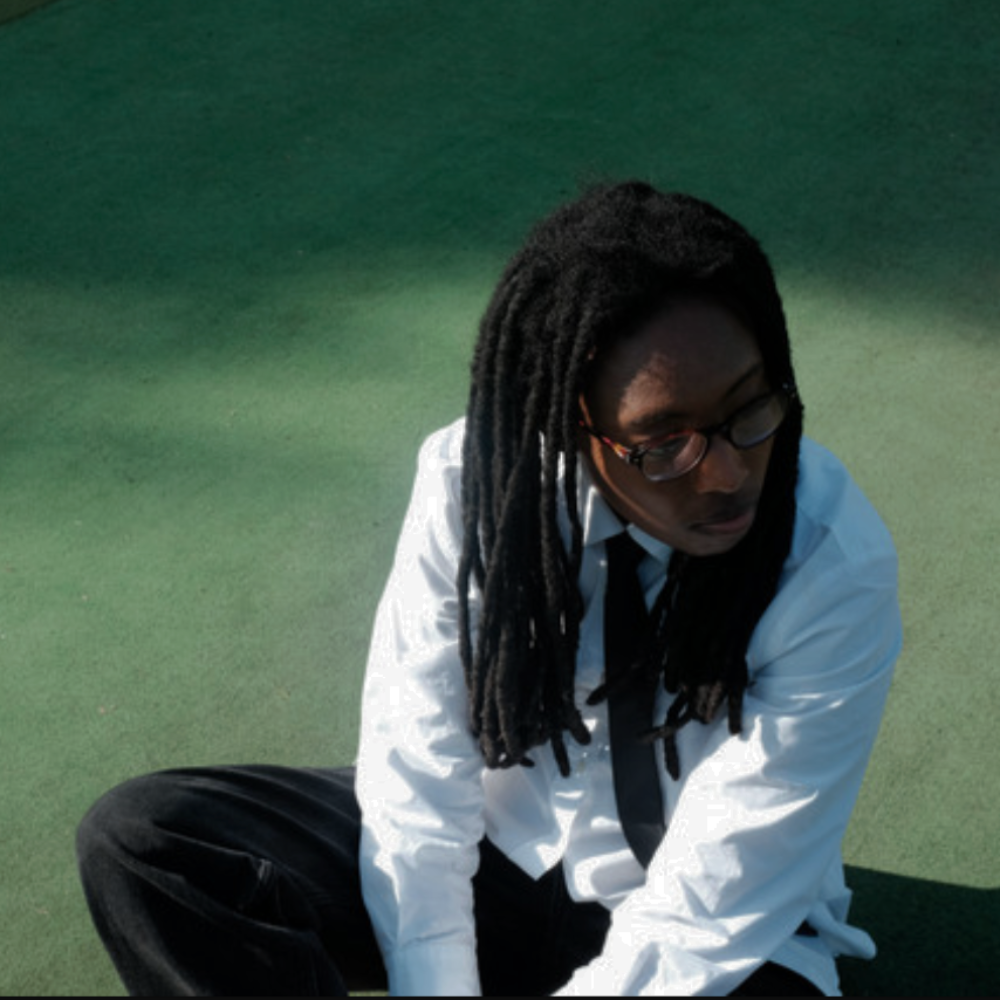 The Gaslight artist in glasses, white shirt and tie, sitting on green ground