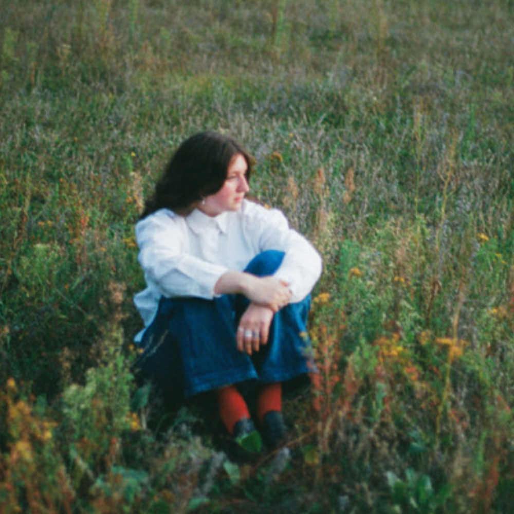 Woman in a white shirt and jeans sitting in long grass