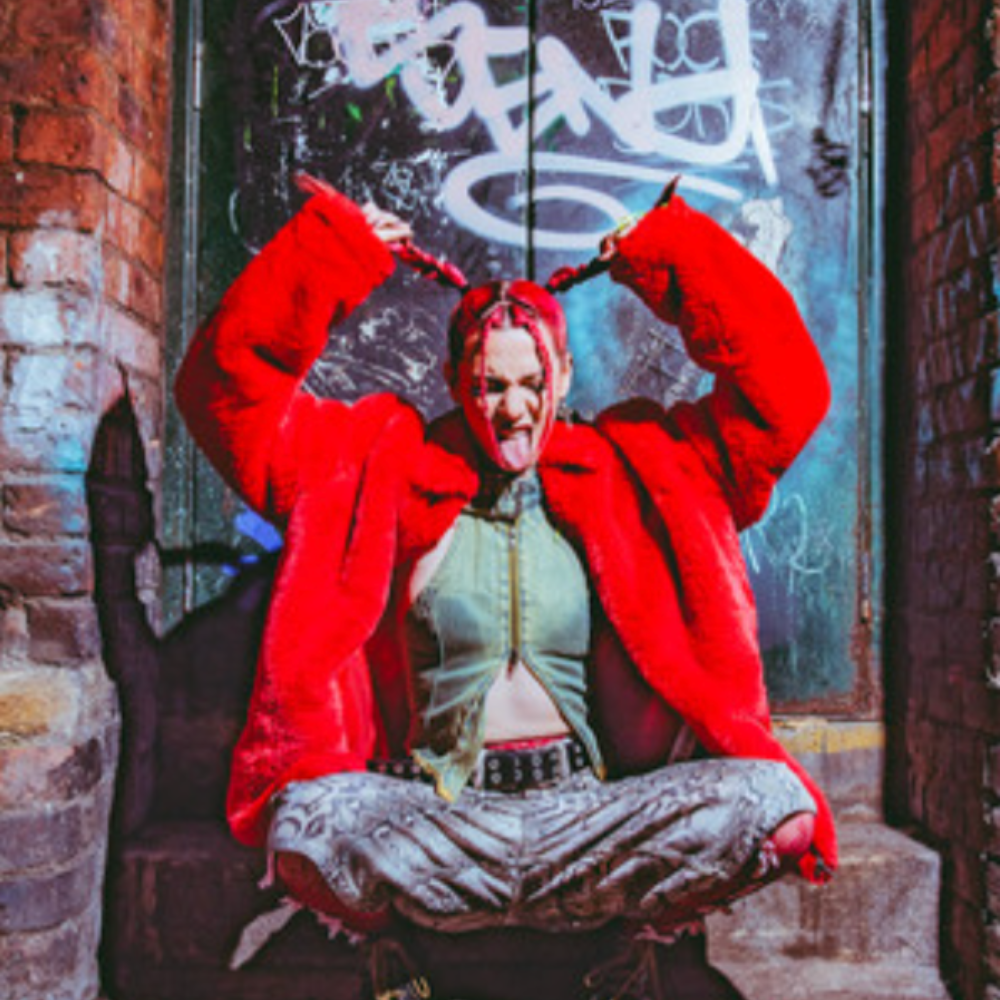 Fleur in a red fur coat, sticking her tongue out in a graffiti-covered doorway