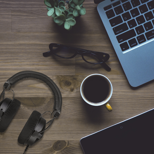 Beyerdynamic DT 770 PRO wired headphones on a wooden desk next to coffee and glasses