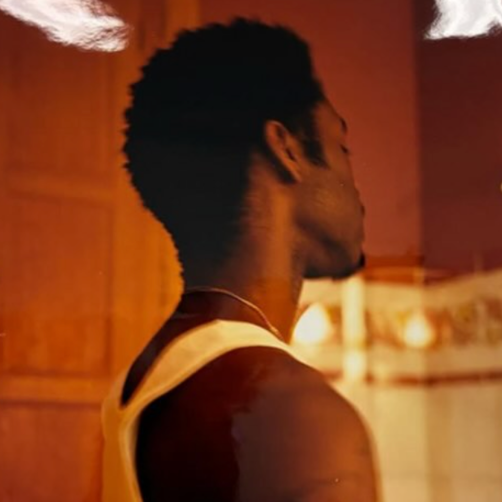 Man in profile in a white vest, lit in warm orange