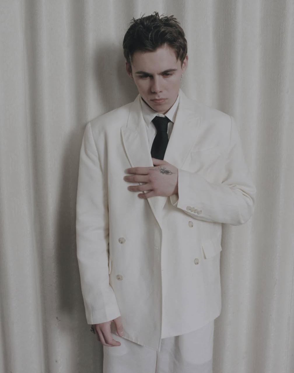 The Kid LAROI in a cream suit and black tie against a curtain