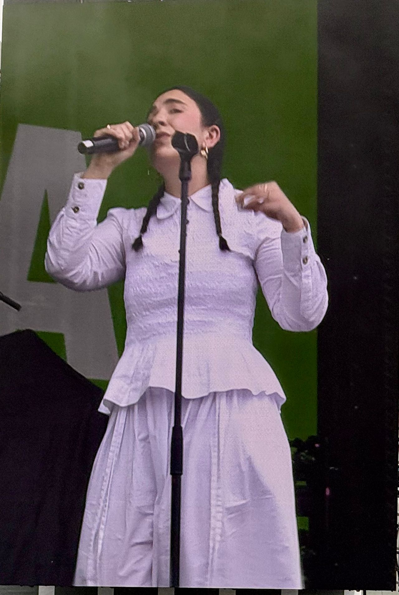 Morgana singing on an outdoor festival stage in a white dress with long braids