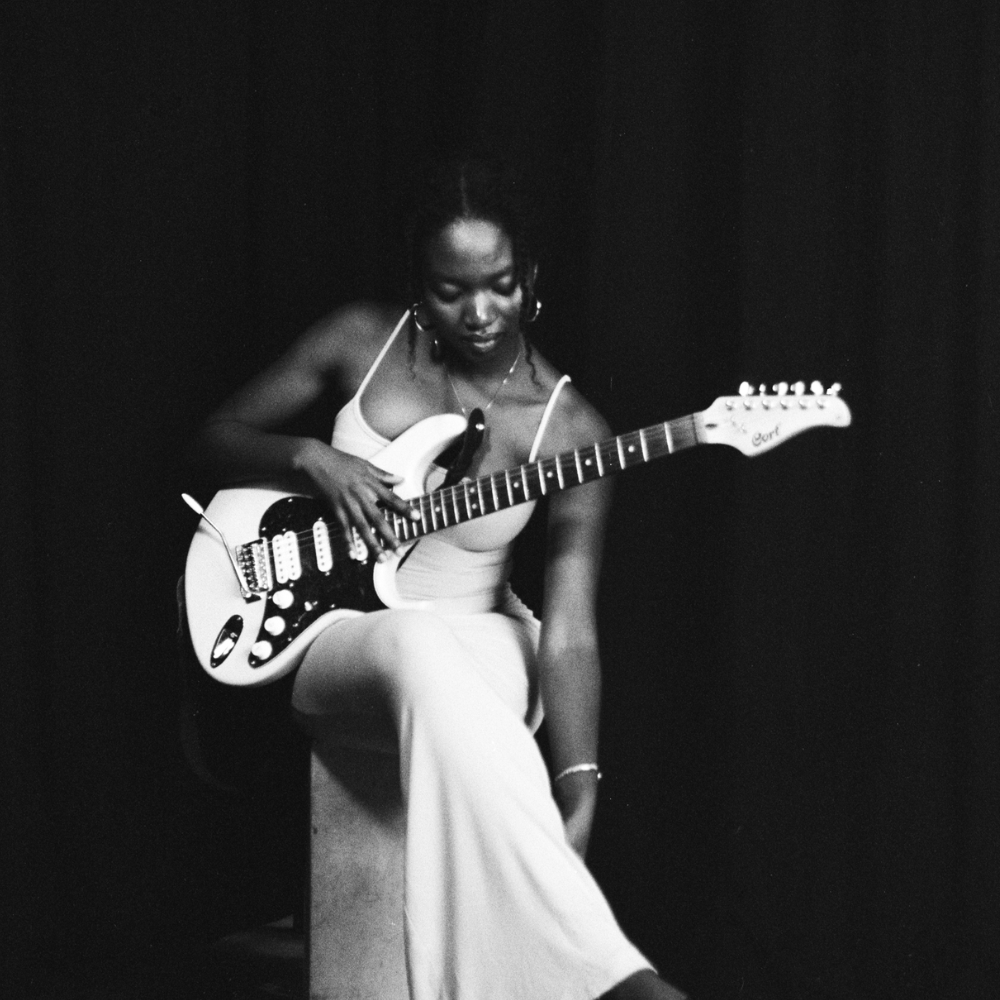 KEZA in a white dress holding a white electric guitar, black and white