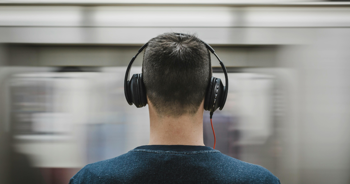 Man in headphones, seen from behind, as a train rushes past