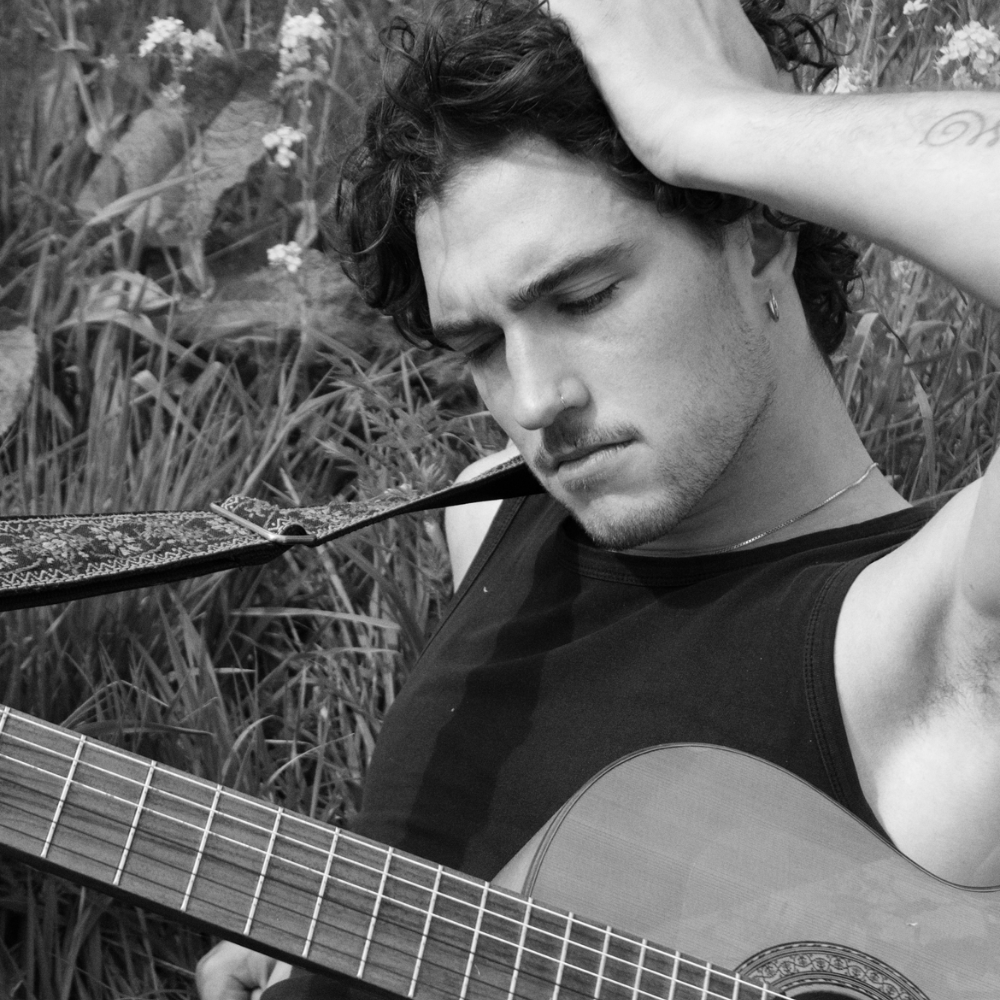 Martim holding an acoustic guitar, hand in his hair, in black and white