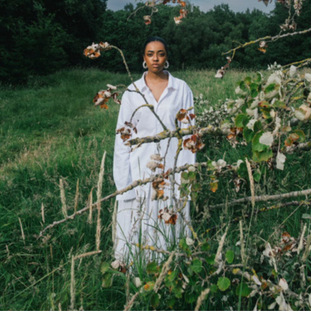 Sarah Isabella in a white shirt dress standing in long grass