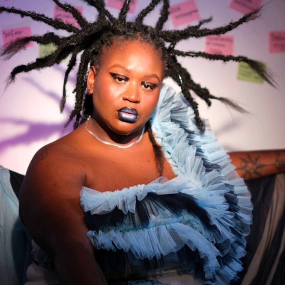 The artist behind Memories, in a ruffled blue dress with sculpted locs