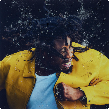 Album cover - a man in a yellow jacket bursting through shattered glass