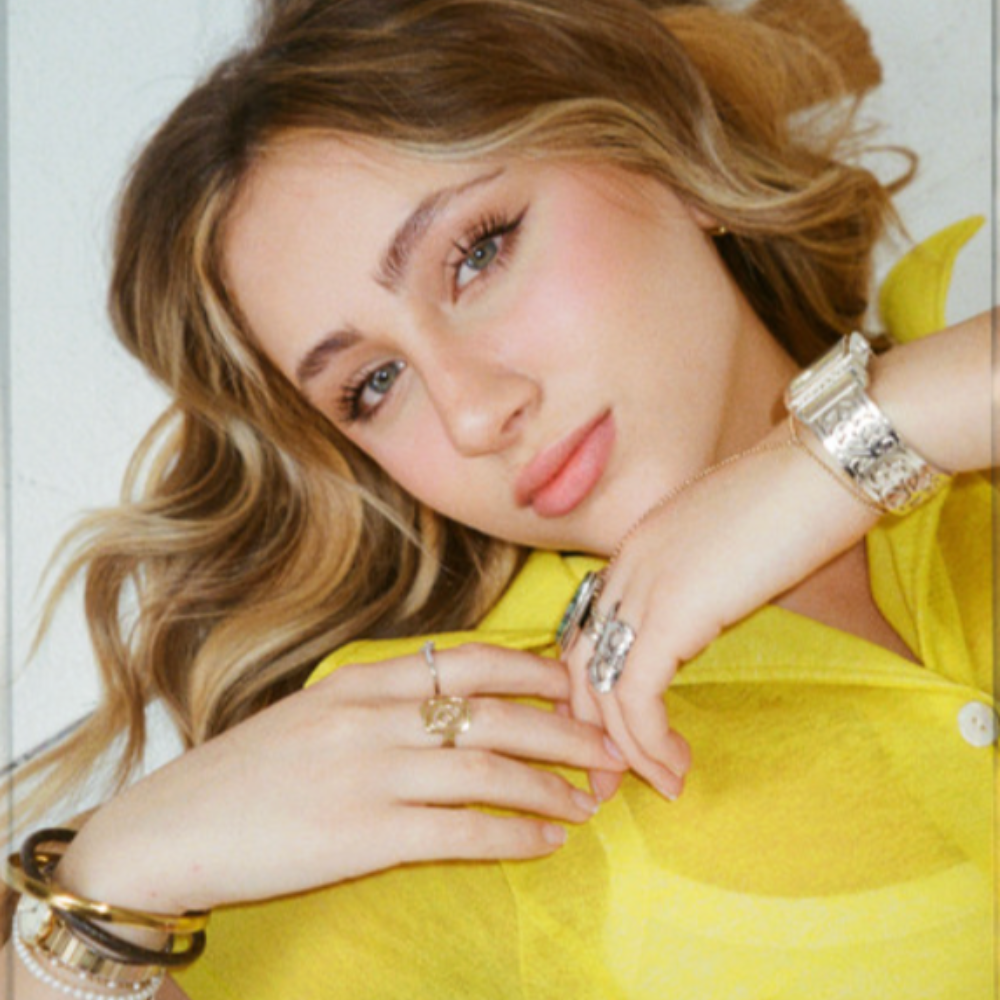 Ava Kolker in a yellow shirt, resting her chin on her hand