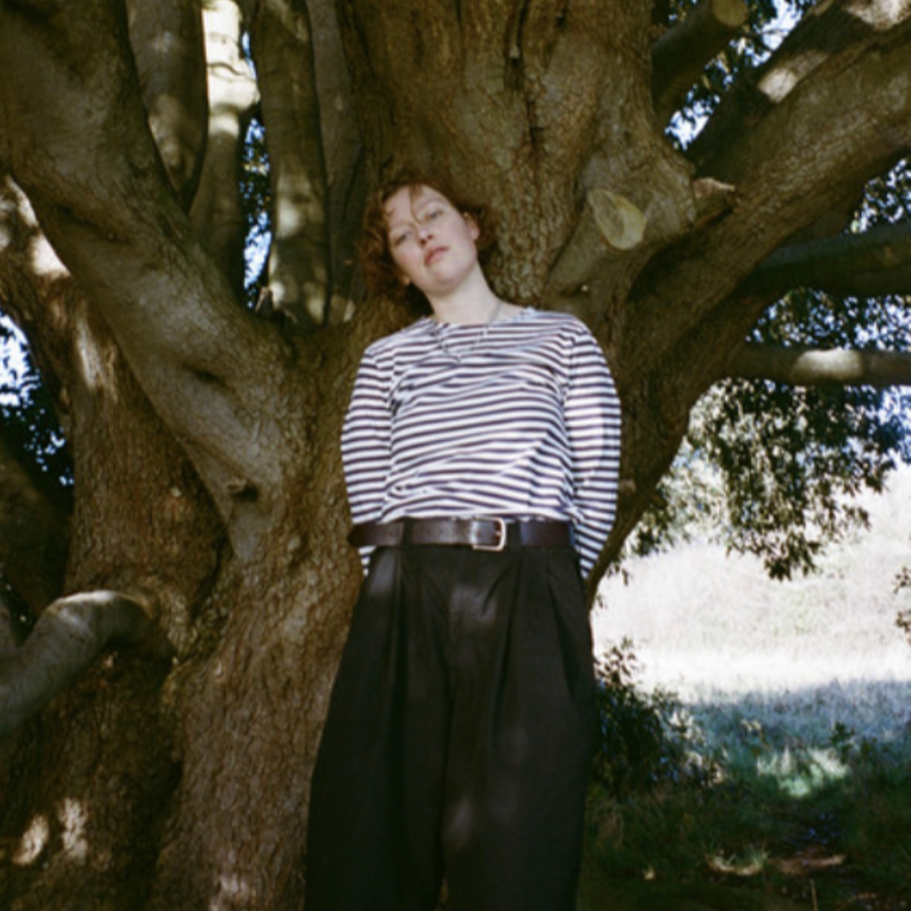 Fran in a striped top, leaning against a large tree trunk