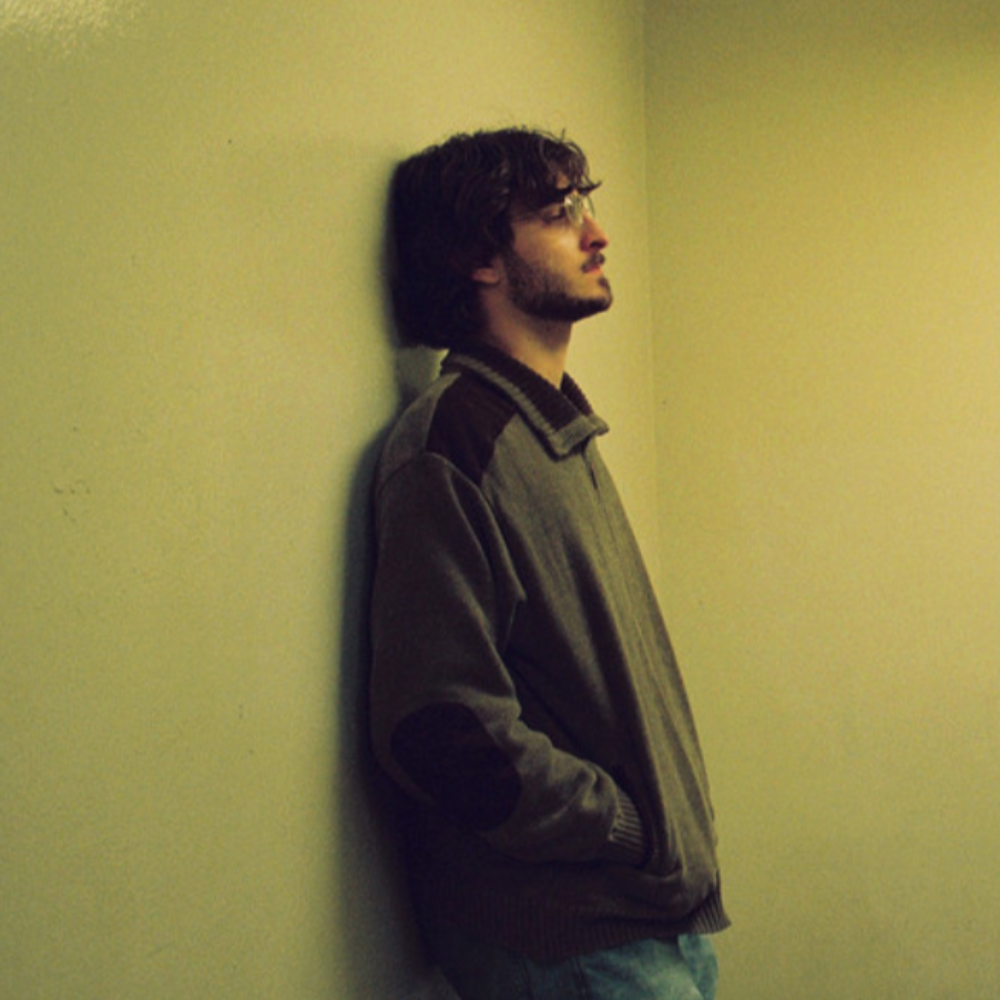 Kerri leaning against a yellow wall, looking away