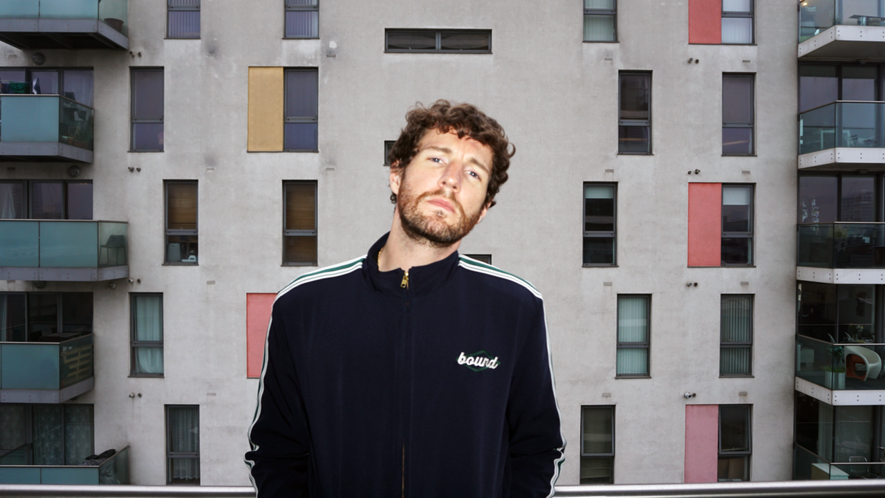 Portrait of a man in a navy track jacket in front of a block of flats