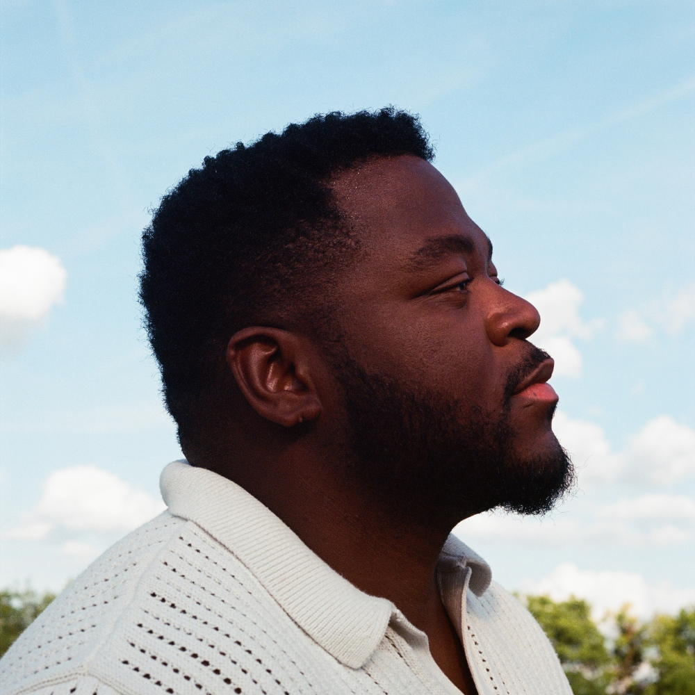 Man in profile in a white knit shirt against a blue sky