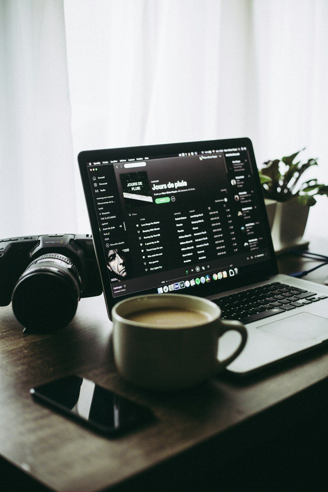 Laptop open on a Spotify playlist next to a coffee cup, camera and phone