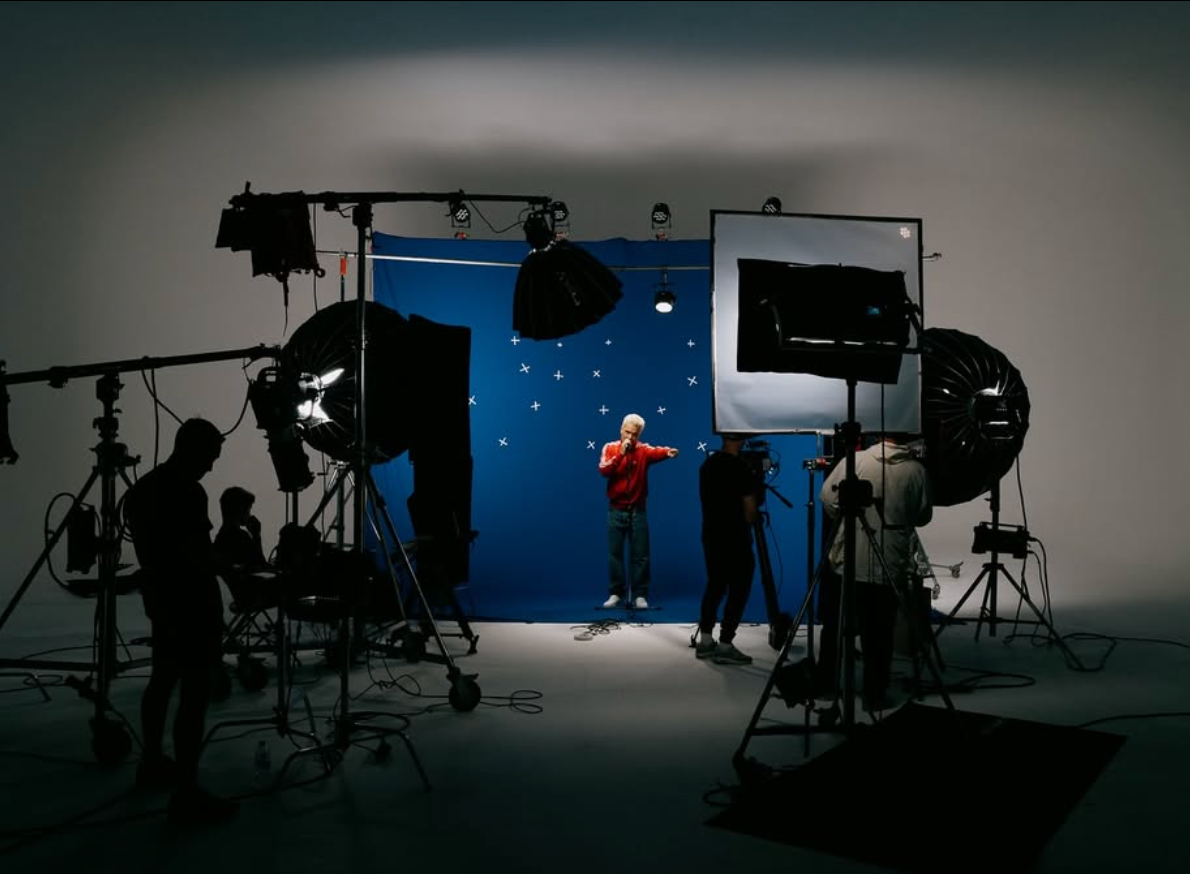 Robbie Williams on a blue-screen film set, surrounded by lights and crew