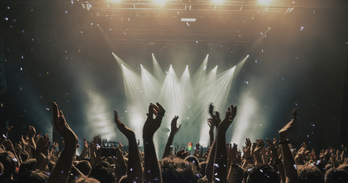 Concert crowd with raised hands under stage lights, for the piece on whether live music is only for the rich