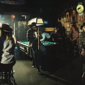 Single cover showing a dim country bar with people in cowboy hats round a pool table