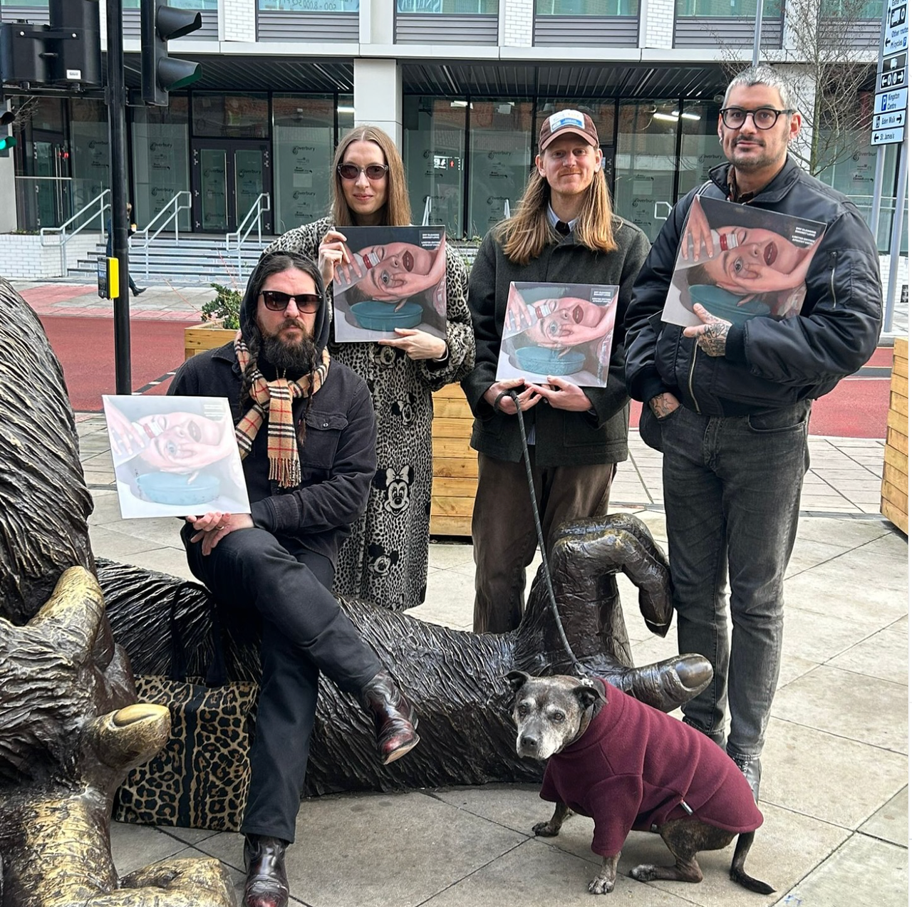 Dry Cleaning holding up copies of Secret Love on a street, with a dog in a jumper
