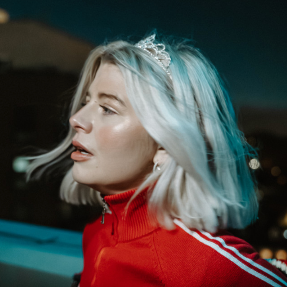 Rachel Newnham with silver hair and a tiara, in a red track top at night