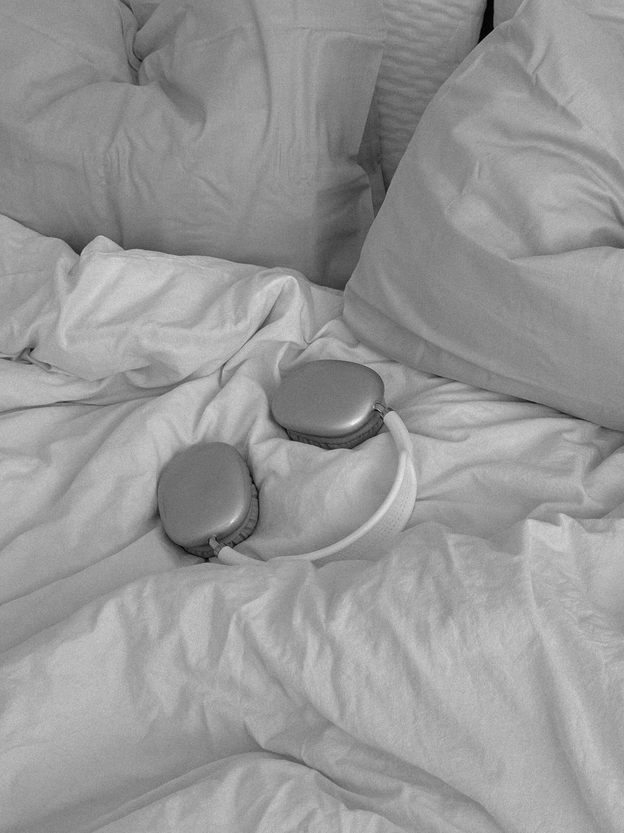 Over-ear headphones lying on rumpled white bedsheets, in black and white
