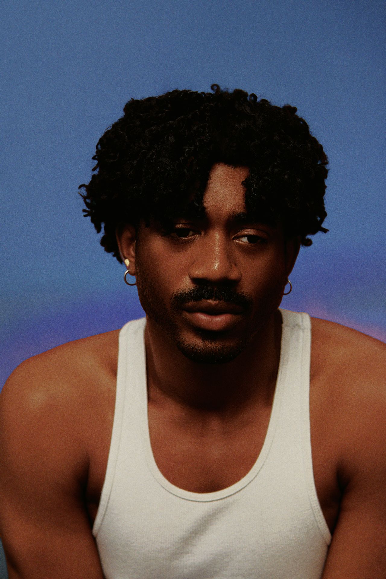 Bronze Avery in a white vest against a blue backdrop
