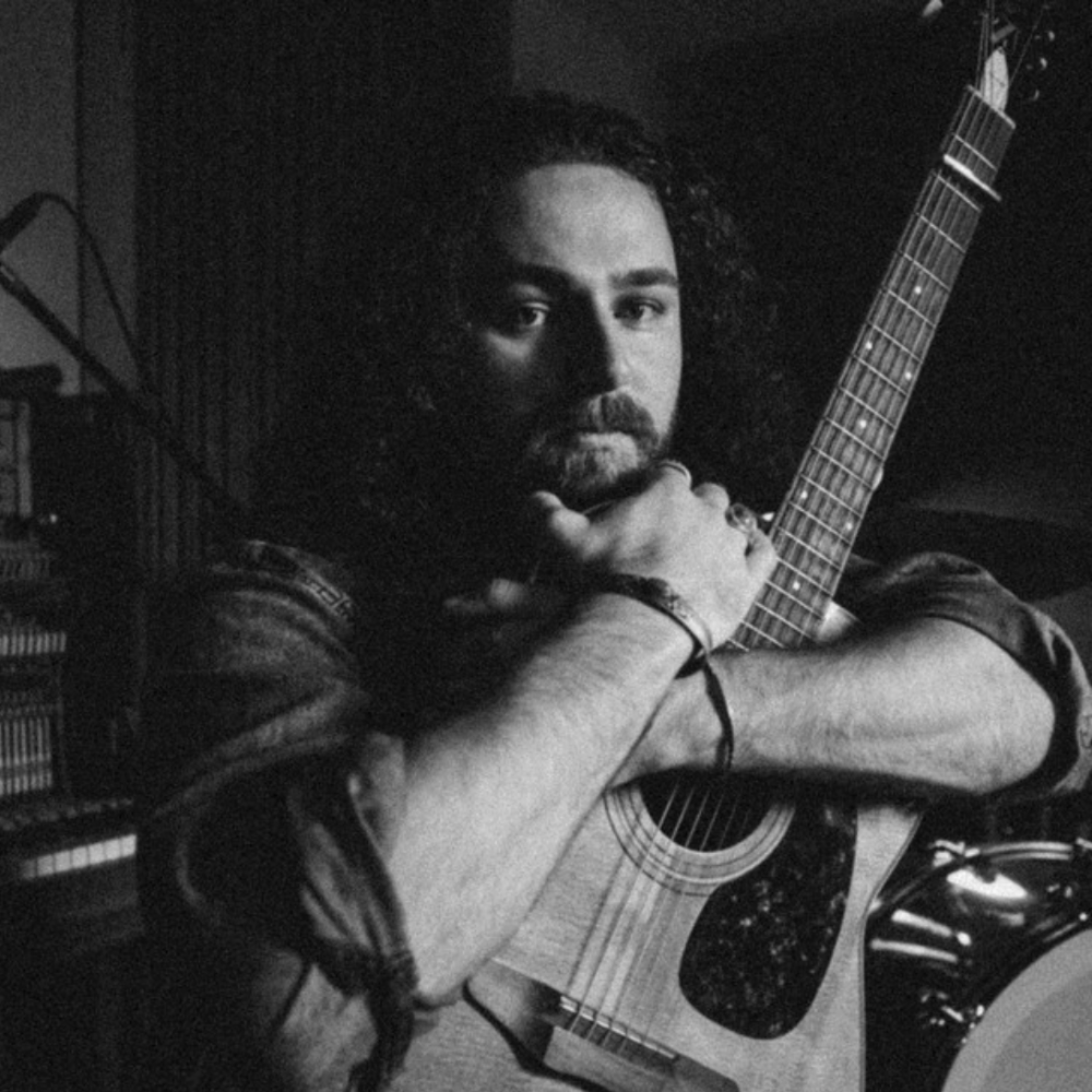 BENNINK holding an acoustic guitar, chin on his hands, in black and white