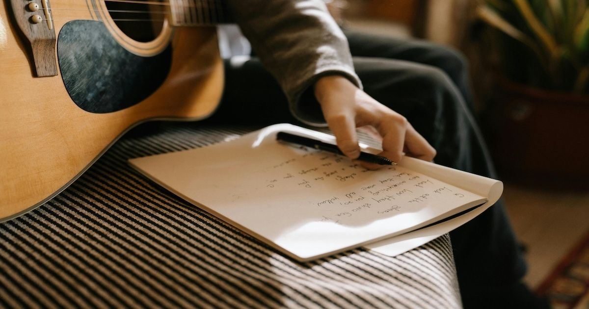 Close-up of a hand turning a page of handwritten lyrics next to an acoustic guitar