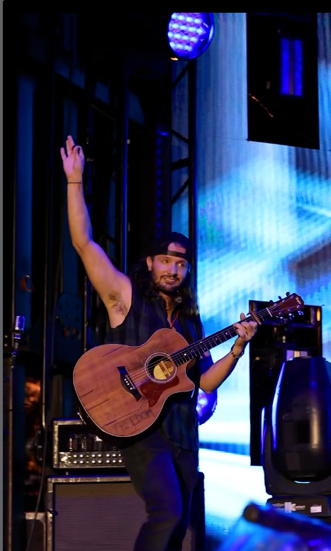 Jutt Huffman on stage with an acoustic guitar, one arm raised